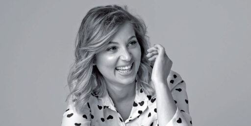 Sourire d'une femme avec cheveux ondulés, portant une chemise à pois, exprimant confiance et bien-être, dans un style professionnel et naturel.