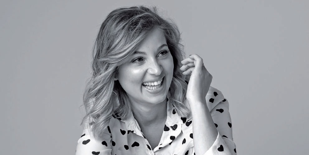 Sourire d'une femme avec cheveux ondulés, portant une chemise à pois, exprimant confiance et bien-être, dans un style professionnel et naturel.