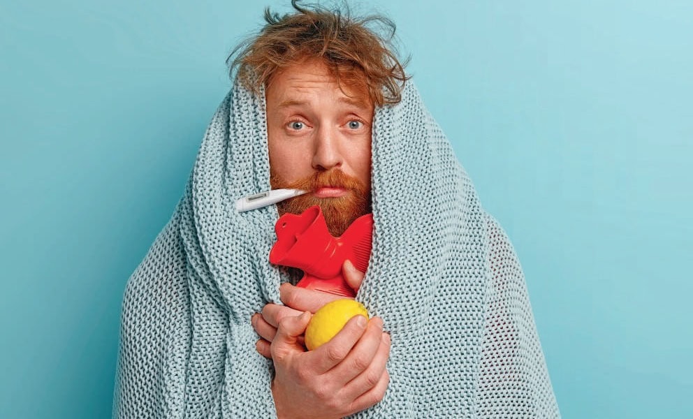 1. Un homme malade avec un thermomètre, enveloppé dans une couverture, tenant un coussin en forme de cœur, symbolisant la fièvre et l'inconfort, sur fond bleu pastel.