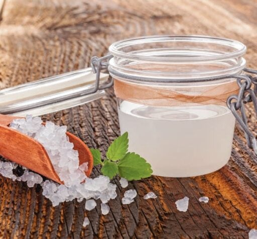 Pot de sel de mer naturel dans un bocal en verre avec une cuillère en bois, sur une surface en bois rustique, idéal pour les soins de santé et la relaxation.
