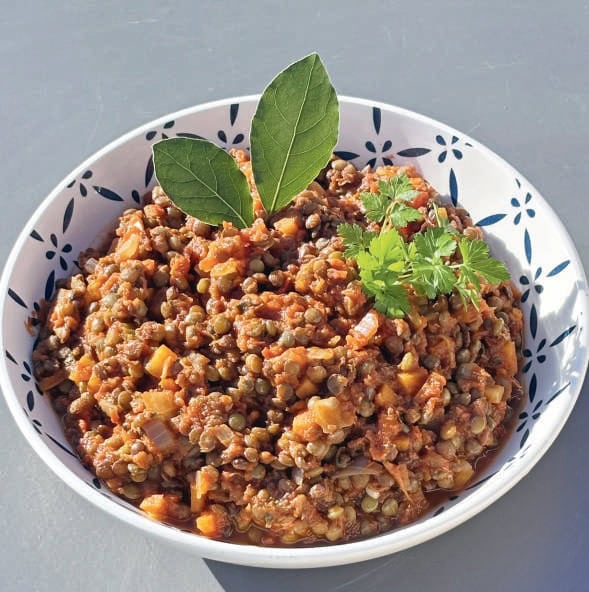 Ragoût de lentilles et légumes bio dans un bol blanc avec des herbes fraîches, idéal pour une alimentation saine et végétarienne.