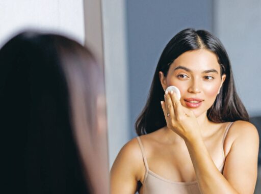 Jeune femme appliquant une crème sur sa joue dans un miroir, illustrant soin de la peau et beauté.