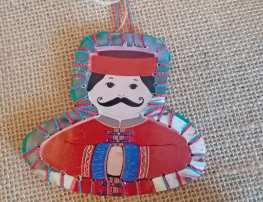 1. Marionnette en papier colorée représentant un cavalier avec chapeau et moustache, décorée de fils multicolores, posée sur une toile de jute.