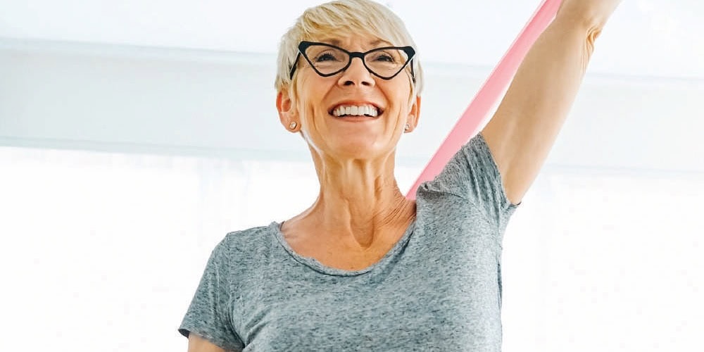 Femme âgée souriante faisant de l'exercice de rééducation avec bande de résistance, pratique de sport pour la santé et le bien-être.