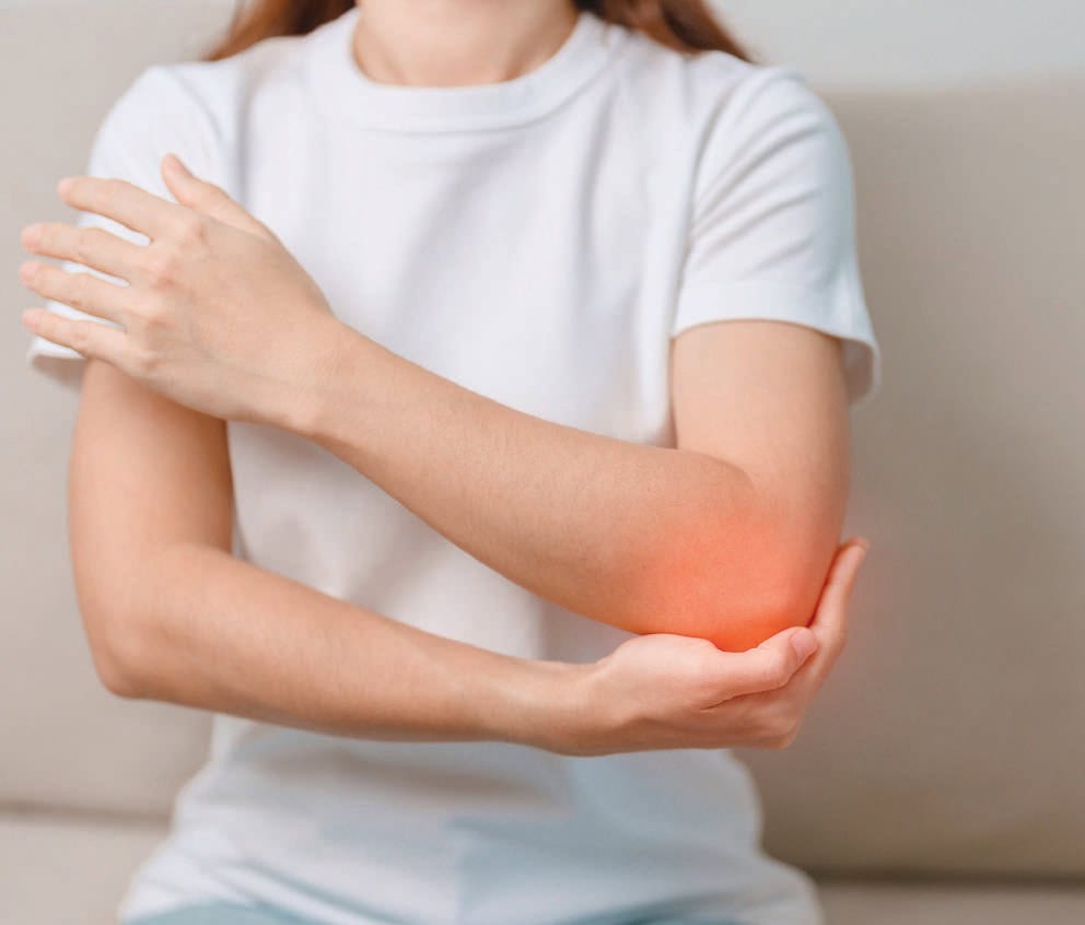 Femme souffrant d'une douleur au coude avec inflammation, illustrant un problème musculo-squelettique nécessitant une attention médicale.