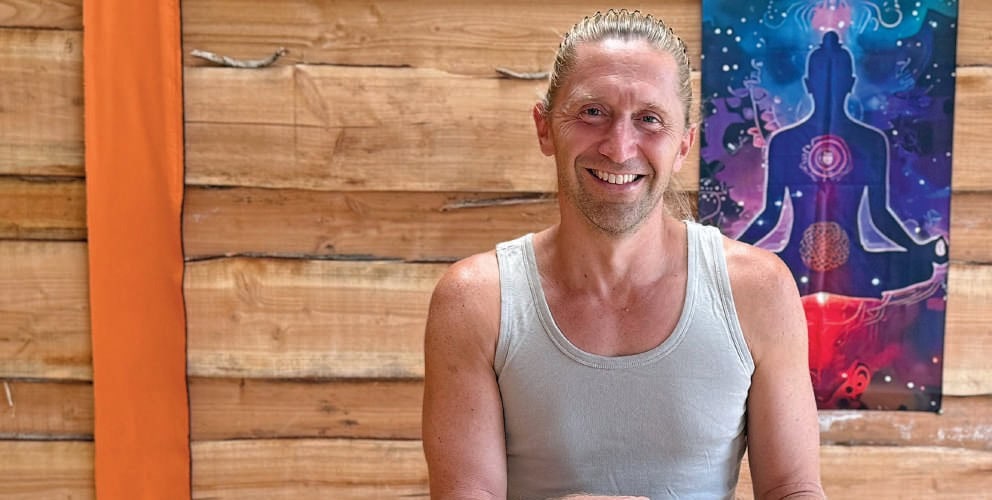 Sourire d'un homme détendu à côté d'une illustration énergétique, ambiance chaleureuse, intérieur en bois, bien-être et équilibre mental, pratique de la santé holistique.